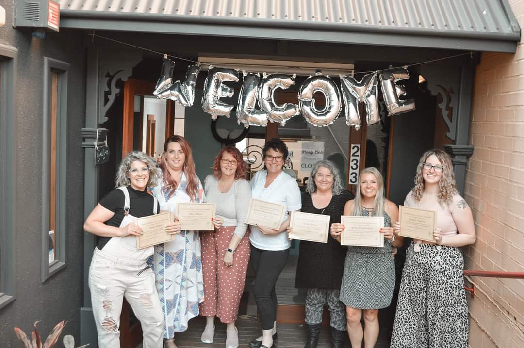 Amanda and some students standing out the front of Purely Curls salon holding their certificates after their course intensive.